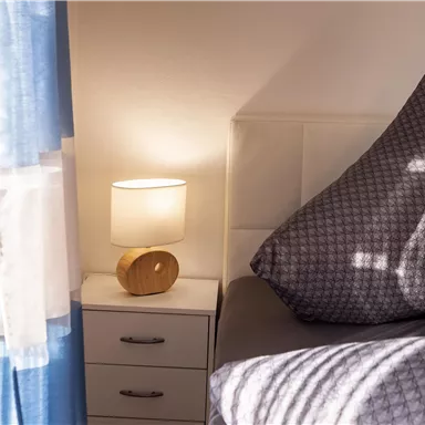 A stylish bedroom with a large pillow and a nightstand. Next to the nightstand stands an elegant lamp that provides soft light.