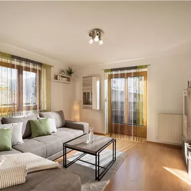 A modern living room with a gray sofa and a coffee table. Large windows provide plenty of daylight and an inviting atmosphere.