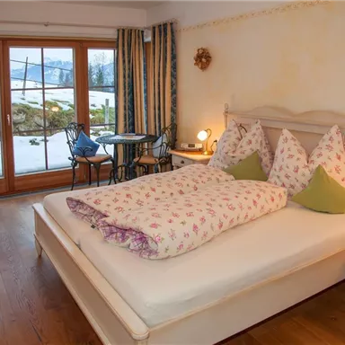 Ein gemütliches Schlafzimmer mit einem großen Bett und Blumenbettwäsche. Durch die Fenster sieht man eine schöne Aussicht auf die Berge und den Schnee draußen.