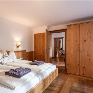 A cozy bedroom with a double bed and wood-paneled walls. There is a wardrobe and soft towels on the bed.