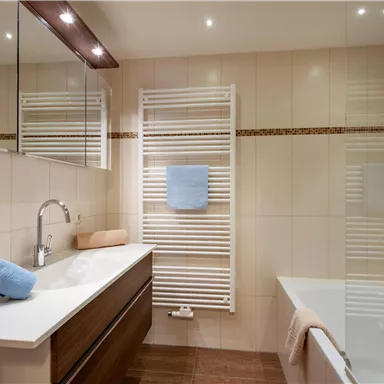 A modern bathroom with a bathtub and elegant wooden cabinets. Towels in soft colors are ready, and large mirrors reflect the light.