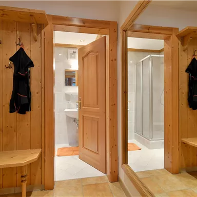 Ein gemütlicher Eingangsbereich mit Holzvertäfelung und einem Spiegel. Im Hintergrund ist ein Badezimmer mit Dusche sichtbar.