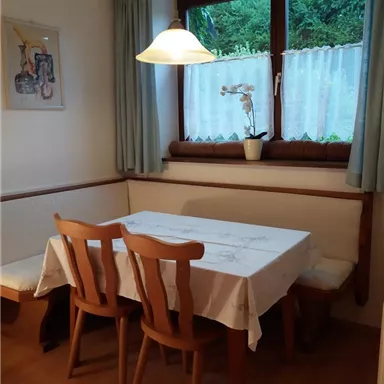 A cozy dining area with a table and four chairs. The room has a window overlooking greenery and a plant decoration.