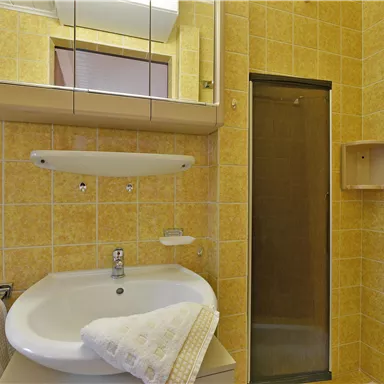 A small bathroom with orange tiles. There is a sink, a mirror, and a shower.