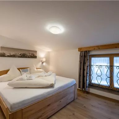 A cozy bedroom with a double bed and wooden furniture. Large windows bring natural light into the room.