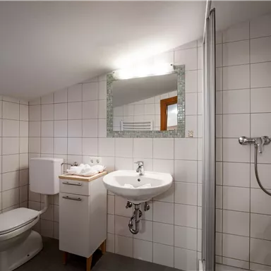 A modern bathroom with white tiles. It features a shower, a sink, and a toilet.