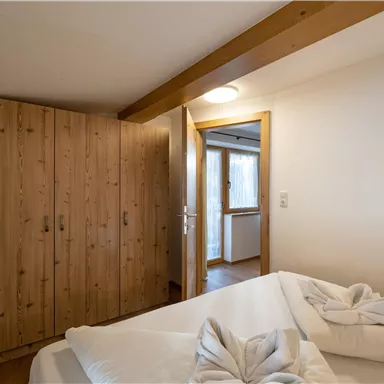 A cozy bedroom with a wooden cabinet and a view of a bright window front. The bedding is carefully folded.