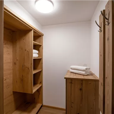 A simple changing room with wooden shelves and towels. Several coat hooks are hanging on the wall.