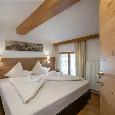 A cozy bedroom with a large double bed and wooden paneling. The warm colors and natural light create an inviting atmosphere.