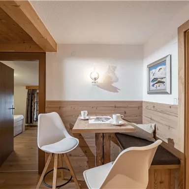 A cozy dining area with a table and white chairs. The walls are paneled with wood, and there is a picture on the wall.
