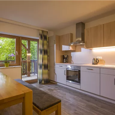 Eine moderne Küche mit Holzschränken und einer großen Fenstertür. Das Licht kommt durch die Fenster und sorgt für eine helle, einladende Atmosphäre.