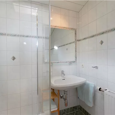 A modern bathroom with a shower and a sink. The walls are tiled and there is a large mirror.