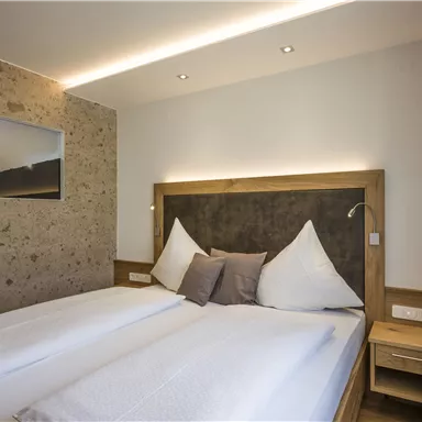 Ein modernes Schlafzimmer mit einem Doppelbett und klaren Linien. Es gibt einen großen Spiegel und eine warme Farbpalette.