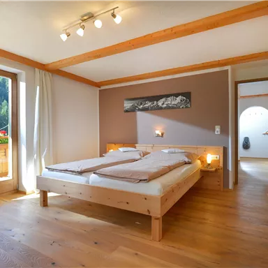 Ein gemütliches Schlafzimmer mit zwei Betten und Holzdecken. Große Fenster lassen viel Licht herein und bieten einen Blick auf die Natur.