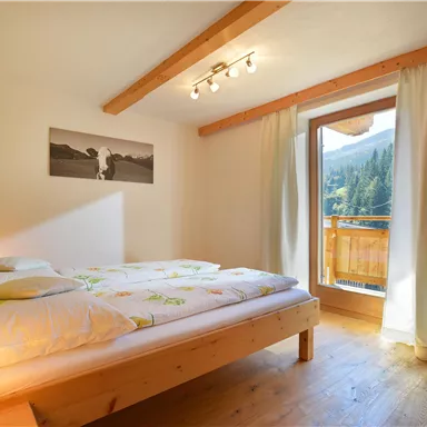Ein gemütliches Schlafzimmer mit einem Doppelbett und Holzverkleidung. Eine große Fensterfront bietet einen Blick auf die Berge.
