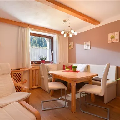 Ein gemütlicher Essbereich mit einem quadratischen Holztisch und hellen Stühlen. An der Wand hängen dekorative Bilder und der Raum ist gut beleuchtet.