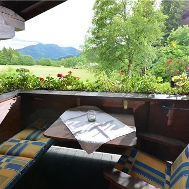 Eine gemütliche Terrasse mit Sitzgelegenheiten und einem Tisch. Im Hintergrund sind grüne Wiesen und Berge zu sehen.