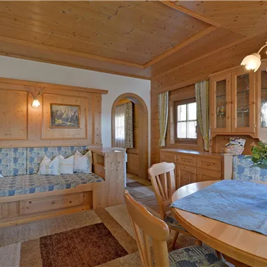 A cozy living space with wooden paneling and an inviting sitting area. A round table with a floral arrangement and a window that lets in natural light.