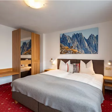 A modern hotel room with a large double bed and a cozy atmosphere. On the wall hangs a picture of mountains, which enhances the natural feel of the space.