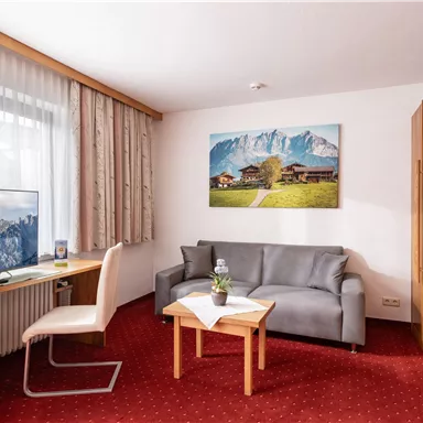 A modern room with a gray sofa, a table, and a television. On the wall hangs a picture of mountains and a rural landscape.