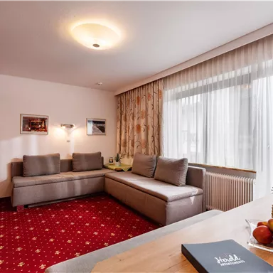 A cozy living room with a gray sofa and a red carpet. Fresh fruit and a guestbook are on the table.