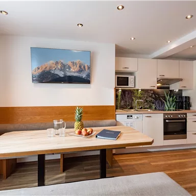 A modern kitchen with a large wooden dining table. In the background, a beautiful landscape nature shot can be seen.