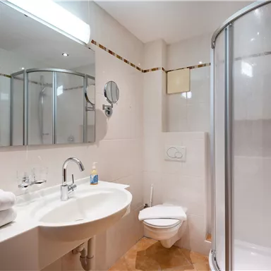 A modern bathroom with a shower, sink, and toilet. The walls are light, and the furnishings are elegant and clean.