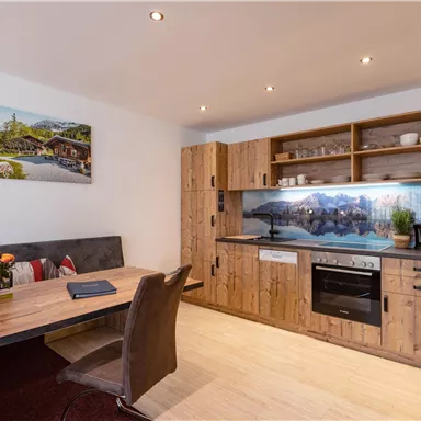 A modern kitchen in wood design with a dining area. The walls are light and there is a picture of a mountain landscape.