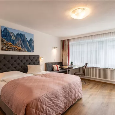 A modern hotel room with a large bed and elegant decor. The room has plenty of natural light and a picturesque wall design.