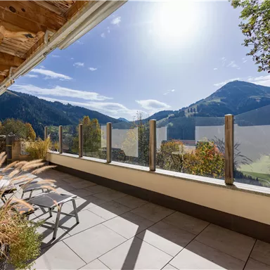 Ein schöner Ausblick von einer Terrasse auf die Berge und die Sonne. Die Umgebung ist grün und einladend, perfekt zum Entspannen.