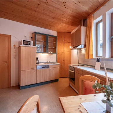 Eine gemütliche Küche mit Holzoberflächen und großen Fenstern. Der Tisch ist mit einer Pflanze dekoriert und sorgt für eine einladende Atmosphäre.