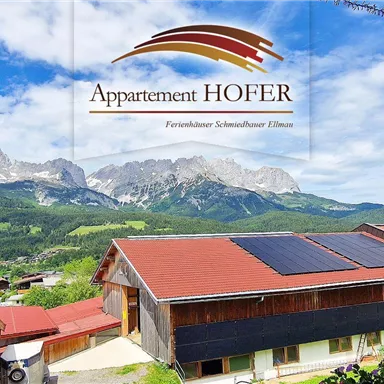 A picturesque view of mountains and a rural panorama. In the foreground, there are houses and a church with a pointed tower.