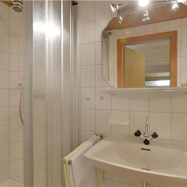 Ein modernes Badezimmer mit einer Dusche und einem Waschbecken. Die Wände sind mit weißen Fliesen ausgestattet und es gibt einen Spiegel.