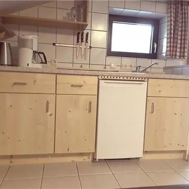 Eine moderne Küche mit Holzschränken und keramischen Fliesen. Sie ist gut ausgestattet mit einem Kühlschrank und verschiedenen Küchenutensilien.