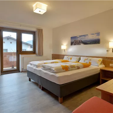 Ein gemütliches Schlafzimmer mit zwei Betten und modernen Möbeln. Große Fenster lassen viel Licht herein und bieten einen Blick nach draußen.