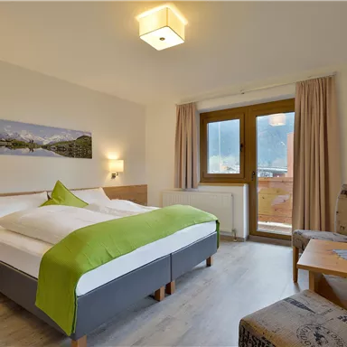Ein gemütliches Hotelzimmer mit einem großen Bett und einem grünen Bettüberwurf. Das Zimmer hat ein Fenster mit Blick auf die Berge und eine einladende Einrichtung.
