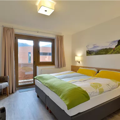 Ein modernes Zimmer mit einem großen Doppelbett und hellem Dekor. Große Fenster bieten Blick auf die Natur und sorgen für viel Tageslicht.