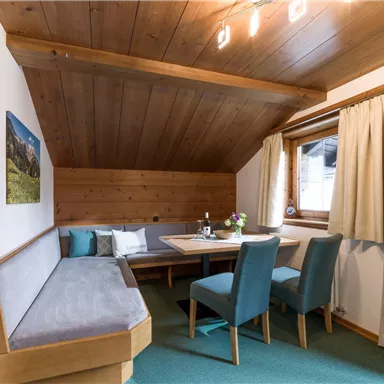 Ein gemütlicher Essbereich mit Holzverkleidung und einem großen Tisch. Die blauen Stühle und der Blick zum Fenster sorgen für eine einladende Atmosphäre.