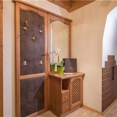 Ein einladender Eingangsbereich mit Holzdekor und einer kleinen Pflanze. Rechts sind gemütliche Möbel in einem hellen Raum zu sehen.