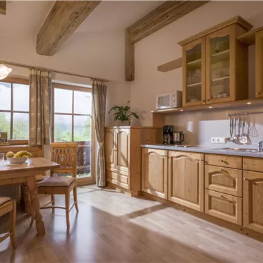 Eine gemütliche Küche im Landhausstil mit Holzmöbeln. Großen Fenstern bietet sie viel Tageslicht und einen Blick ins Grüne.