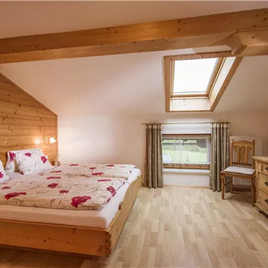 Ein helles Schlafzimmer mit einem Doppelbett und einem Holzinterieur. Ein Fenster mit Dachfenster sorgt für viel Tageslicht.