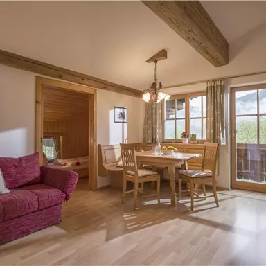 Ein gemütliches Wohnzimmer mit einem roten Sofa und einem Essbereich aus Holz. Großes Fenster mit Blick auf die Natur und ein heller, einladender Raum.