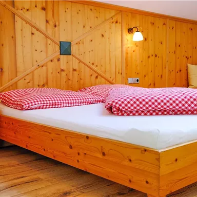Ein gemütliches Schlafzimmer mit einem Holzbett und karierten roten Kissen. Wände aus Holz verleihen dem Raum eine warme Atmosphäre.