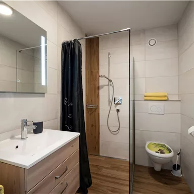 A modern bathroom with a shower and a sink. There are bright tiles and wooden elements, as well as colorful towels.