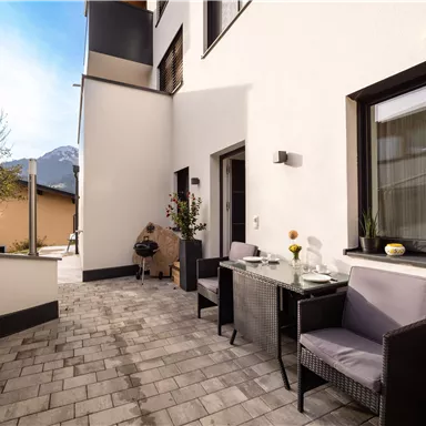 A modern terrace with a table and chairs. In the background, mountains and a clear sky can be seen.