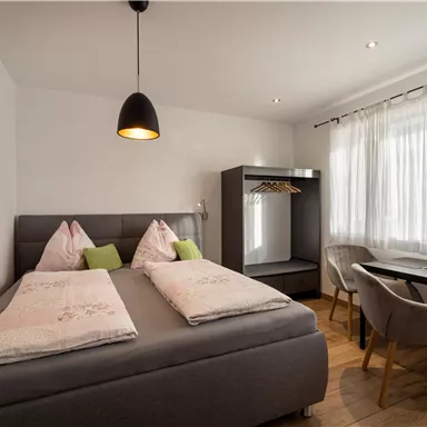 A cozy bedroom with a double bed and modern decor. The room is bright and inviting, featuring a desk and a large window.