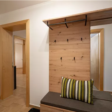 Ein moderner Flur mit Holzelementen und einem bequemen Sitzbereich. Die Wände sind hell und die Türen führen in andere Räume.