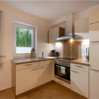 Eine moderne Küche mit hellen Schränken und einer Fensterfront. Die Ausstattung umfasst einen Herd, eine Spüle und eine Kaffeemaschine.