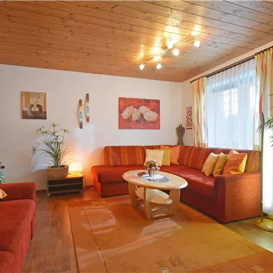 A cozy living room with red sofas and a round table. Warm light and decorative plants create an inviting atmosphere.