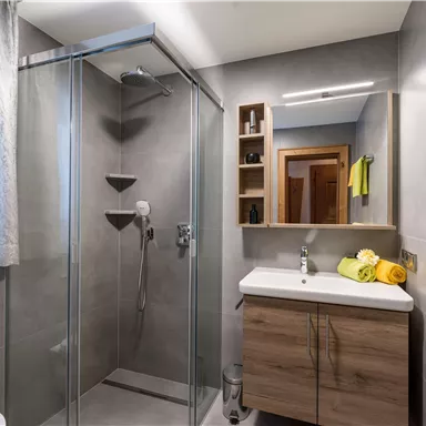 A modern bathroom with a glass shower and a sturdy wooden vanity. Fresh yellow towels and bright window decor create an inviting atmosphere.